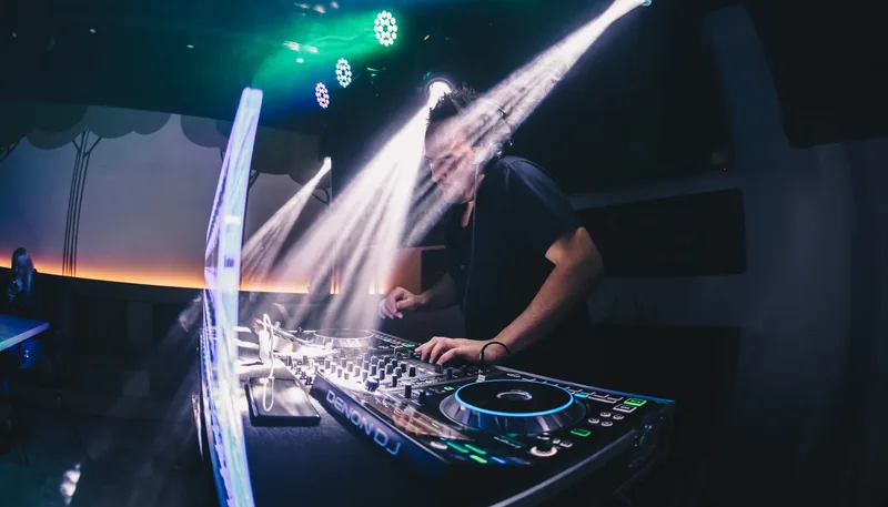 Tomy Vertigo behind the decks amid beams of light.