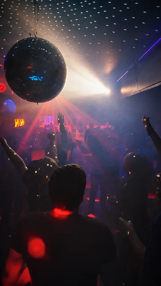 Video cover: a disco ball hangs above dancers with raised arms amid haze and red and white party lights.