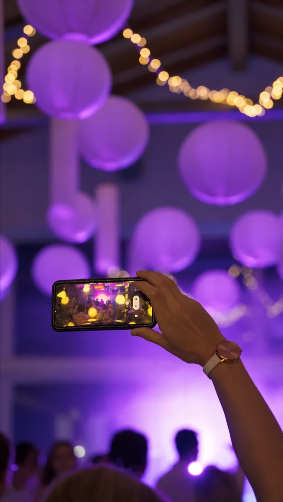 Video cover: a guest films the party on a phone beneath hanging spheres and strings of lights in a purple-lit room.