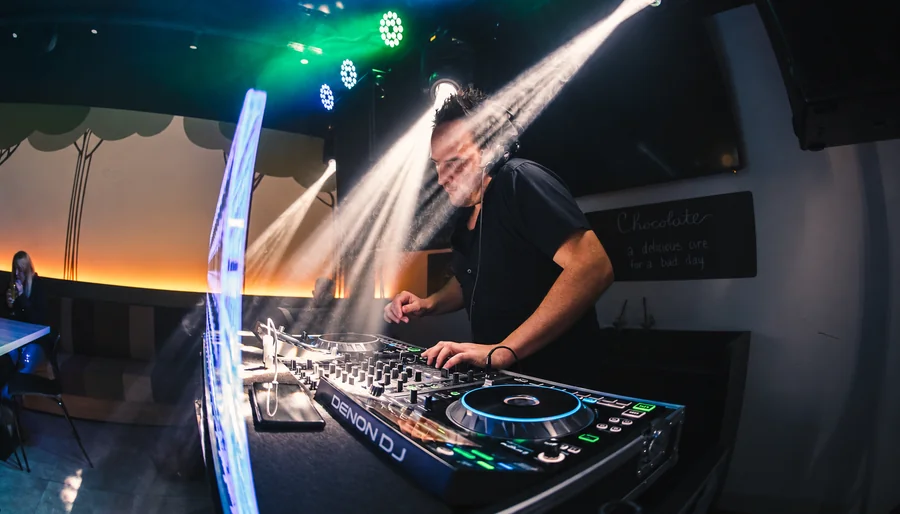 Tomy Vertigo behind the decks amid beams of light.