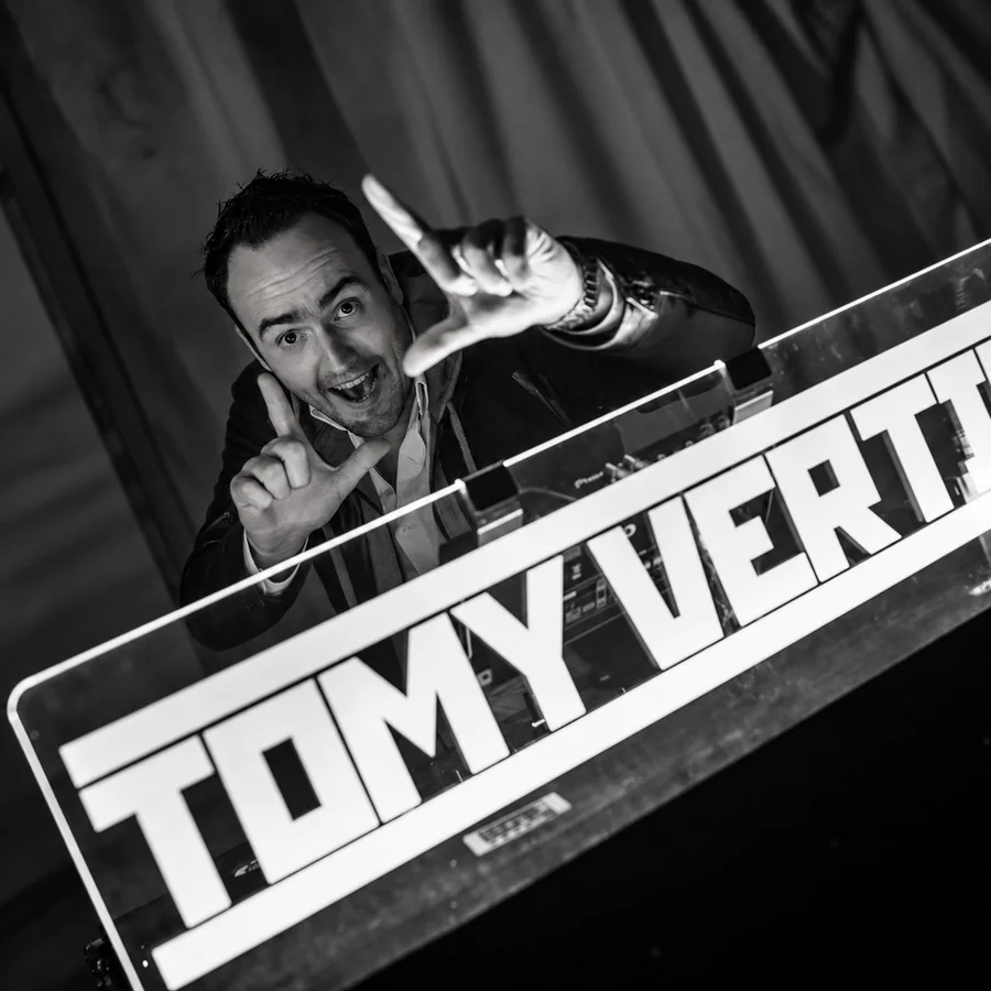 A black-and-white portrait of Tomy Vertigo at the DJ booth.