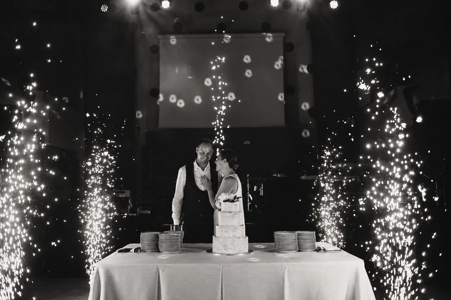 A wedding couple by their cake amid bubbles and sparks.