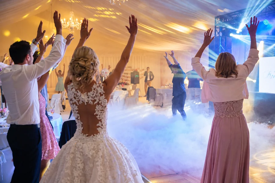A bride and wedding guests with raised hands on the dance floor.