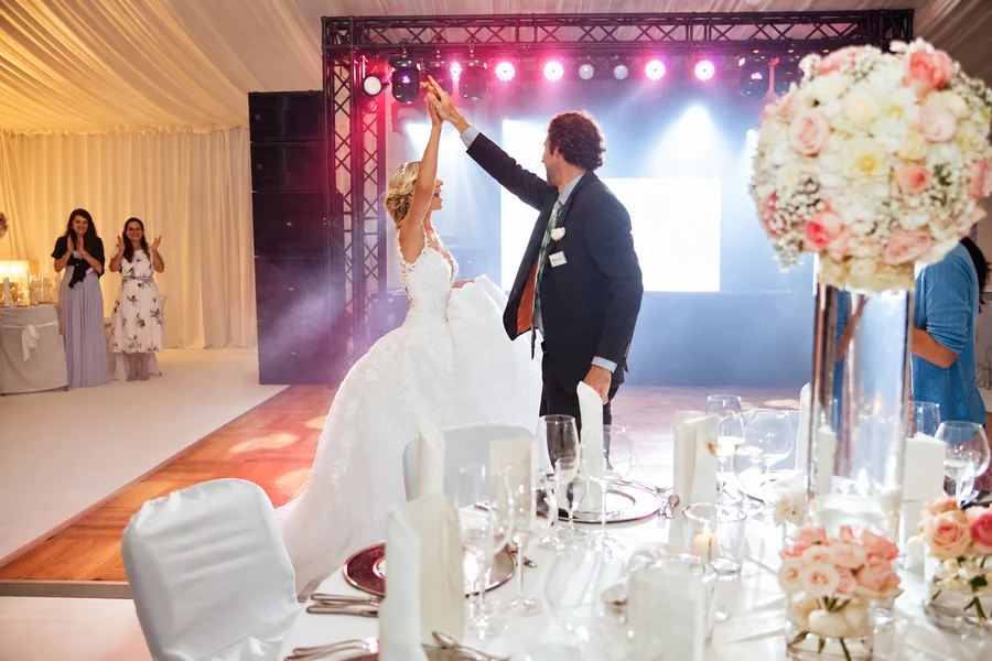 A wedding couple during their first dance beside floral arrangements.