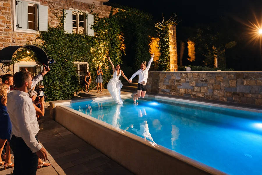 A lively night celebration beside an illuminated pool.