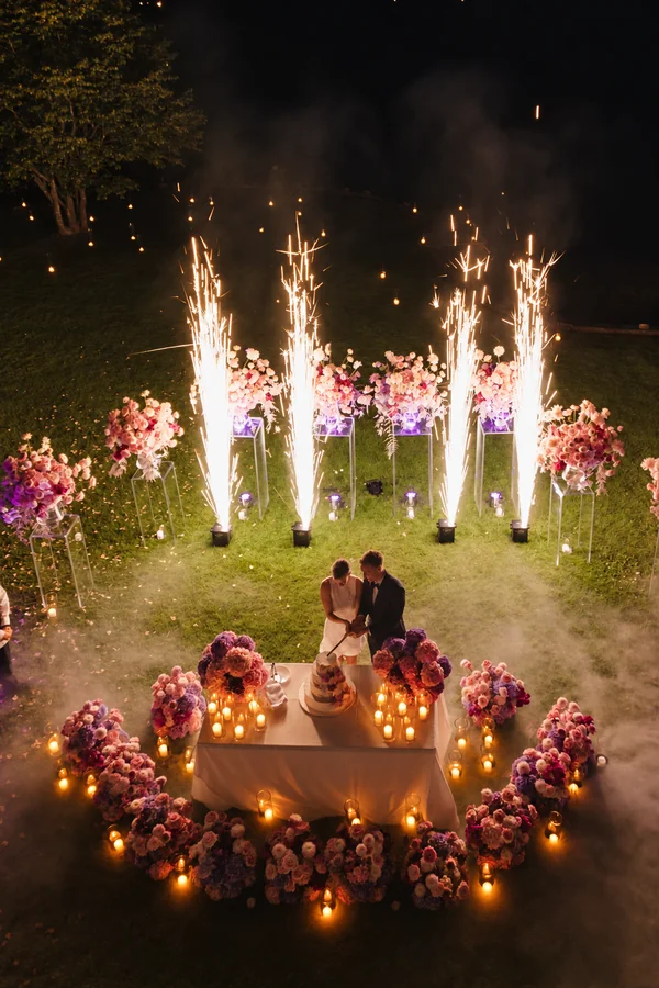 An outdoor wedding moment framed by light sparks and candles.