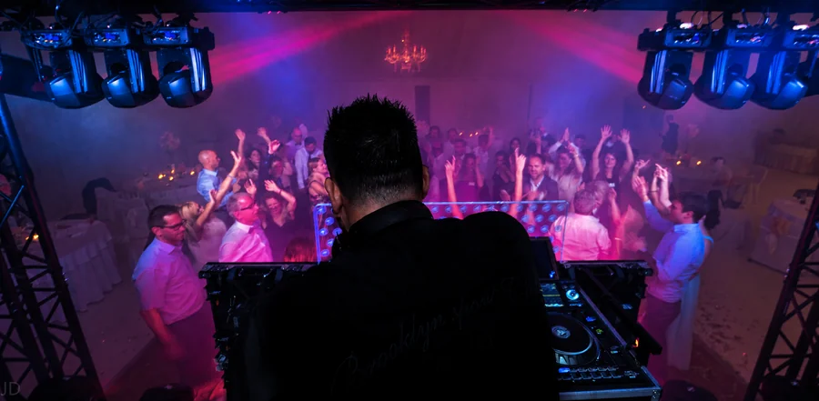 A view from behind the DJ booth towards a full dance floor.